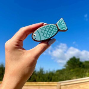 Little fishy in walnut. painted in blue with scales and a face, being held in a hand