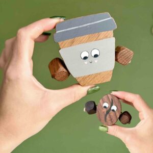 Two wooden toys – a smiling coffee cup made from oak with grey painted details, and a wooden coffee bean made from walnut with a hand-painted swirl, both with dangling arms.